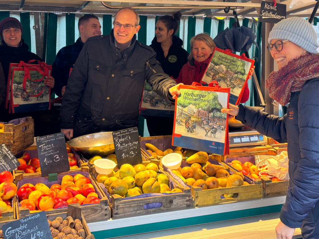 Uebergabe der neuen Markttaschen am Obststand des Harburger Wochenmarkts