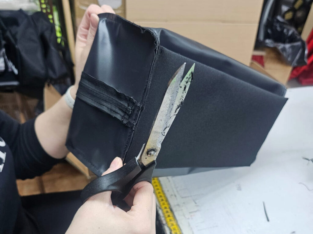 Endkontrolle: Faeden werden an der fertig genaehten Tasche von Hand sauber abgeschnitten
