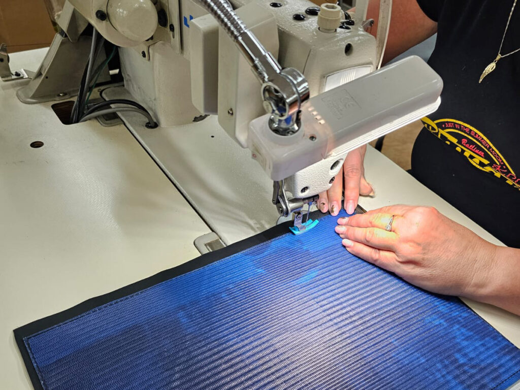 Naeherin fasst die blaue Klappe der Messenger-Tasche an der Industrienaehmaschine ein