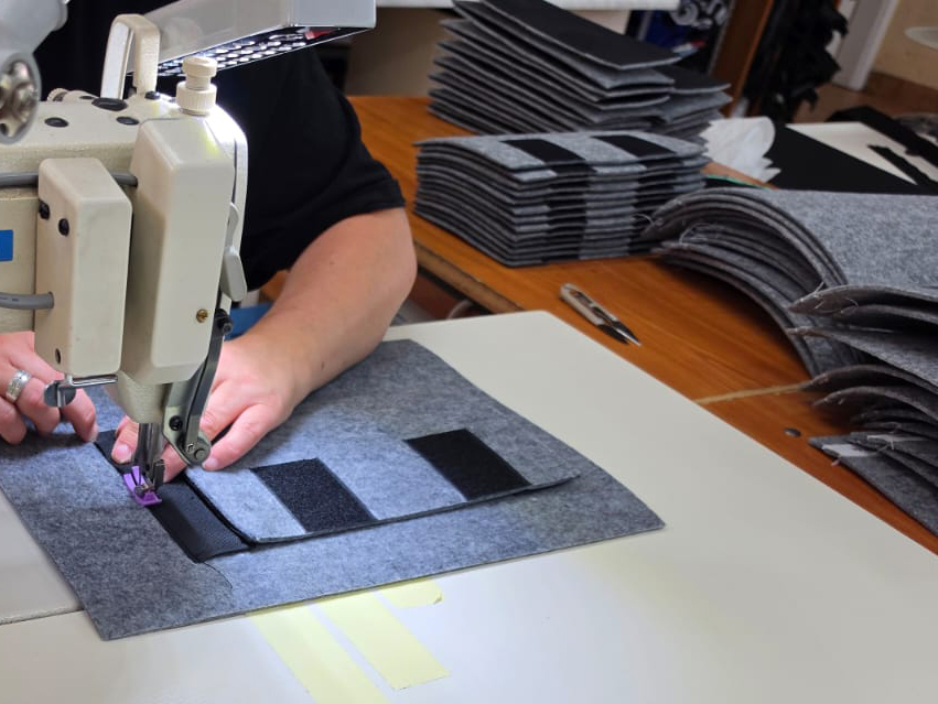 Konfektion an der Naehmaschine, im Hintergrund die vorbereiteten Zuschnitte