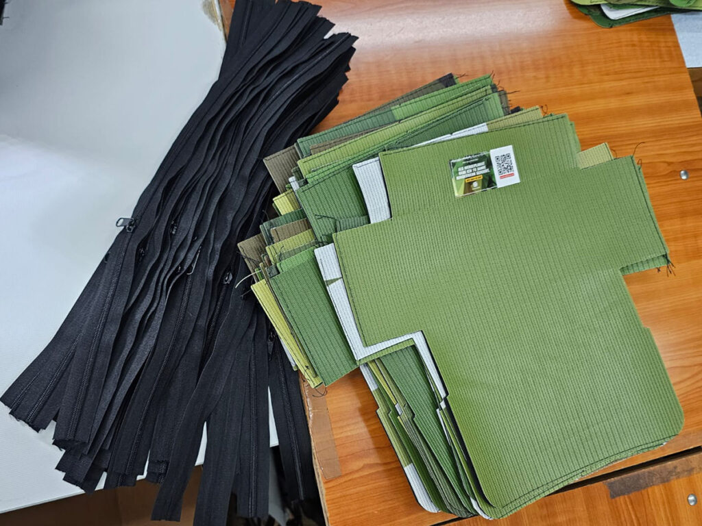 Zugeschnittene Etui-Teile aus recyceltem Plakatstoff neben schwarzen Reißverschlüssen